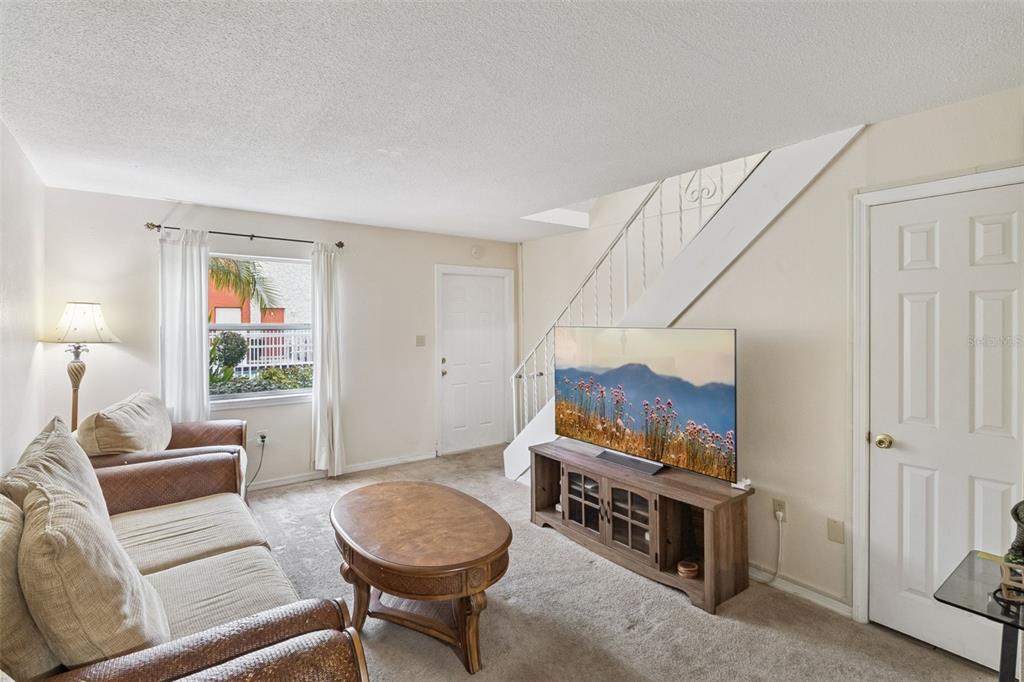 A living room features beige carpet, a sofa, a coffee table, and a television stand — 50 NEEDLE BOULEVARD UNIT 32, MERRITT ISLAND, FL
