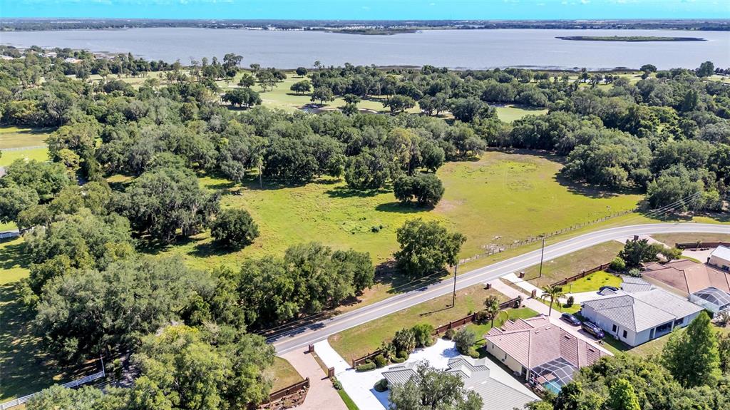 An aerial view shows a large grassy lot bordered by trees, a road, and houses — COUNTRY CLUB ROAD S, WINTER HAVEN, FL