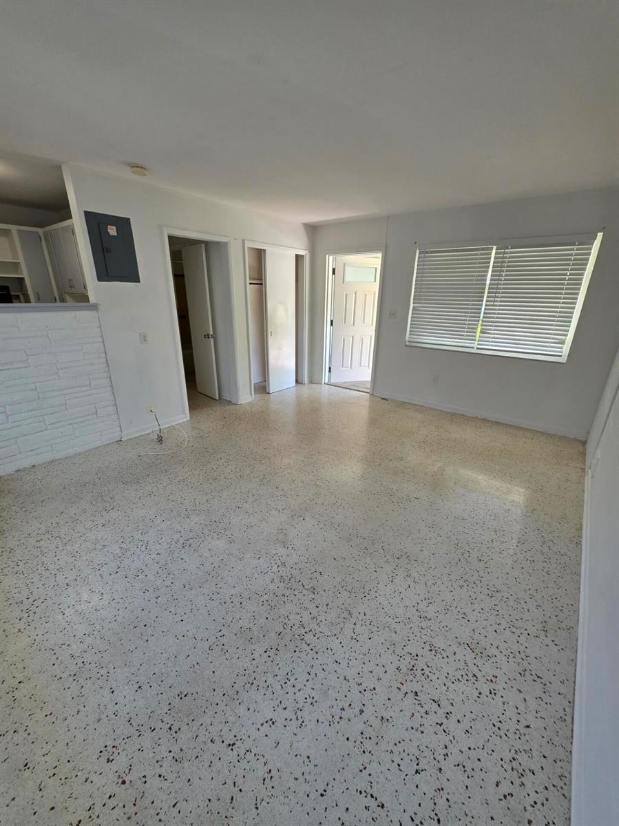 An empty room features white walls, a white brick accent wall, and speckled terrazzo flooring — 1216 Cabana Road # 1a, Singer Island FL 33404, SINGER ISLAND, FL
