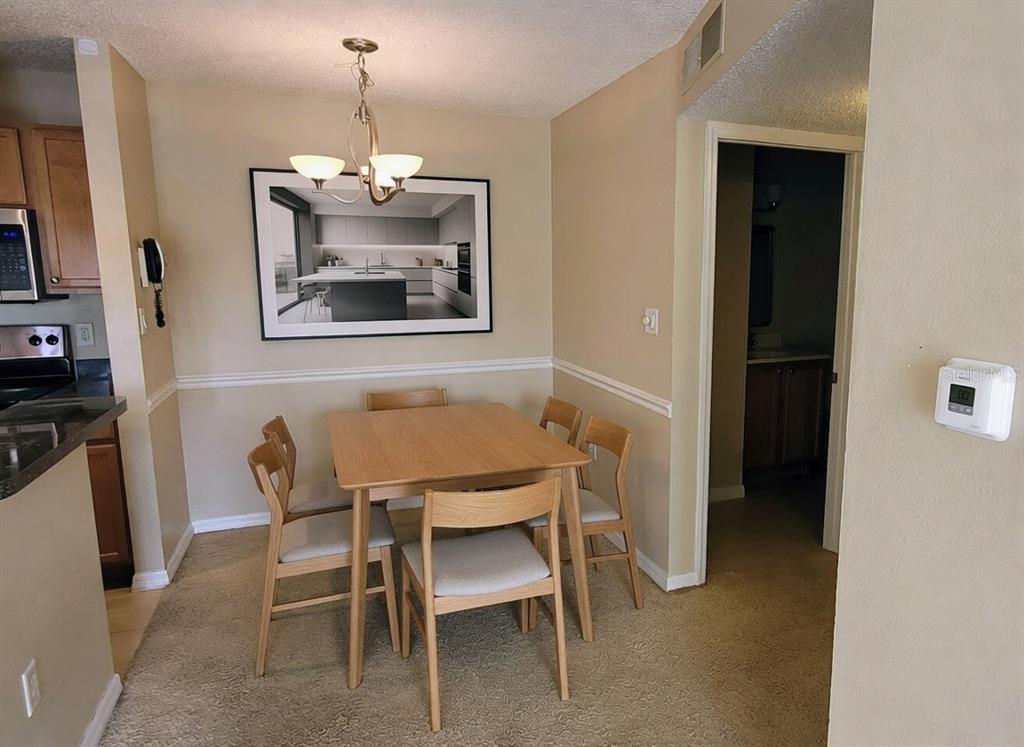 A dining area features a wooden table with four chairs, a chandelier, and carpeted flooring — 302 LAKE PARSONS GREEN UNIT 102, BRANDON, FL