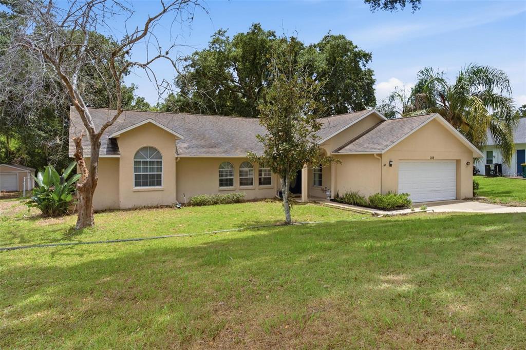 A single-story tan house with a white garage door and a large front yard — 742 WOODVIEW DRIVE, TAVARES, FL