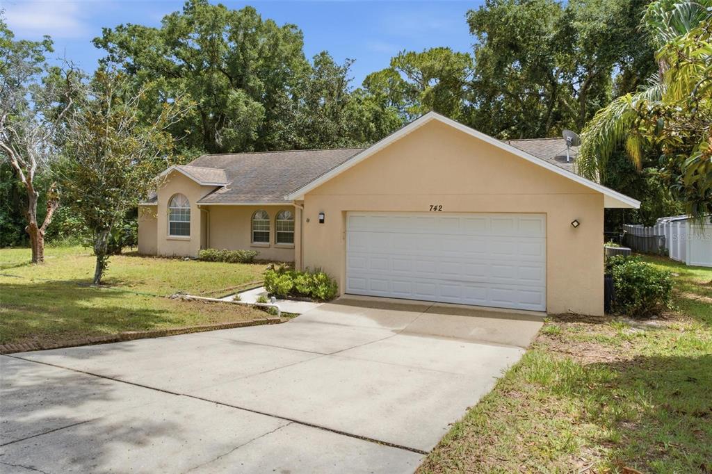 A single-story tan house with a white garage door and a concrete driveway — 742 WOODVIEW DRIVE, TAVARES, FL