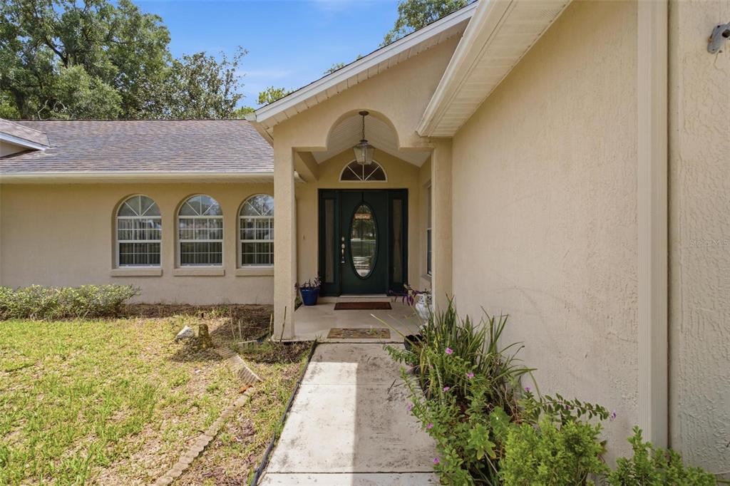 A beige stucco house exterior features an arched entryway, a dark front door, and three windows — 742 WOODVIEW DRIVE, TAVARES, FL