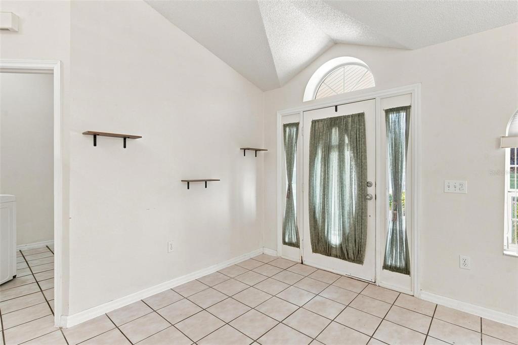 An entryway with tiled floors, vaulted ceilings, three wall-mounted shelves, and a front door — 742 WOODVIEW DRIVE, TAVARES, FL