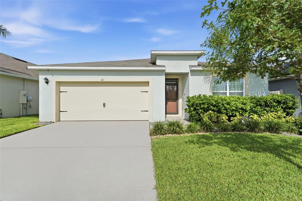 A single-story house with a beige garage, a front door, and a landscaped front lawn — 121 OLD MILL POND ROAD, EDGEWATER, FL