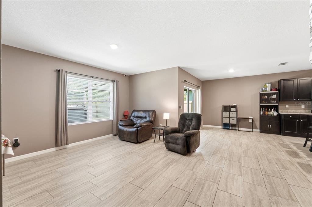 A living area with light wood-look tile flooring, two recliners, and a small wet bar — 121 OLD MILL POND ROAD, EDGEWATER, FL