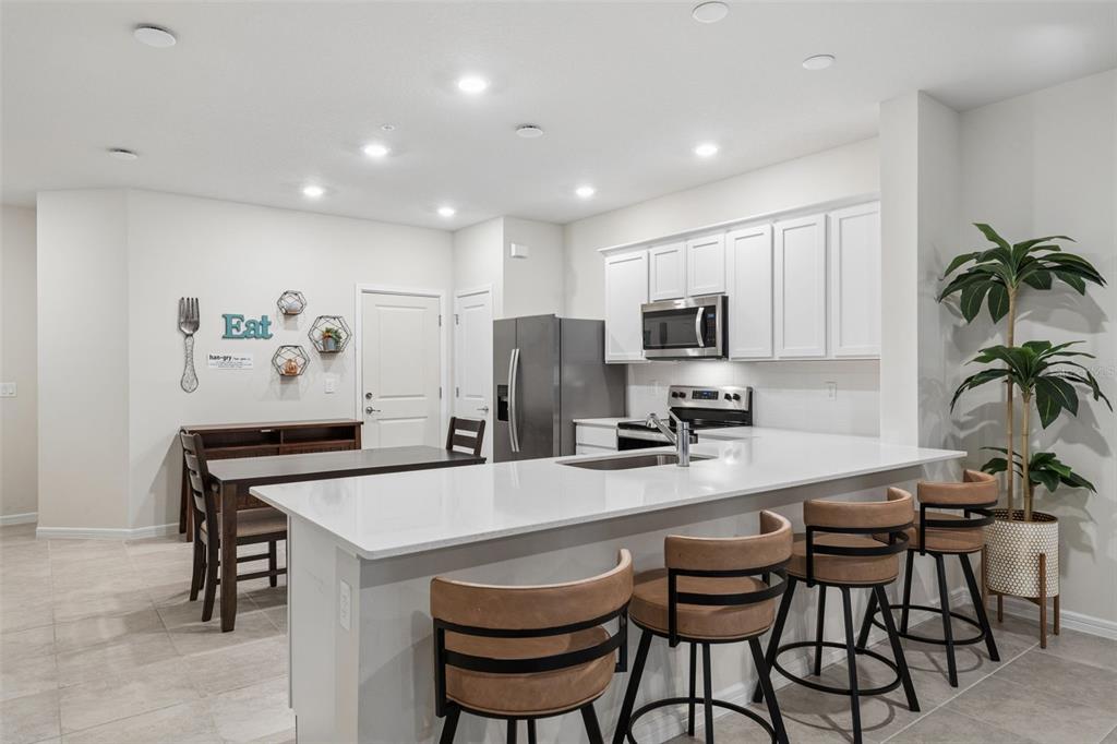 A kitchen features white cabinets, a quartz island with bar stools, and an adjacent dining area — 2017 CANNY COVE, WINTER PARK, FL