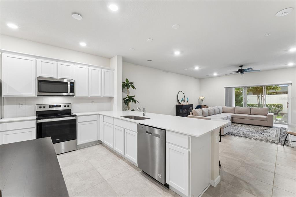 A modern kitchen with white cabinets and stainless steel appliances opens to a living area — 2017 CANNY COVE, WINTER PARK, FL