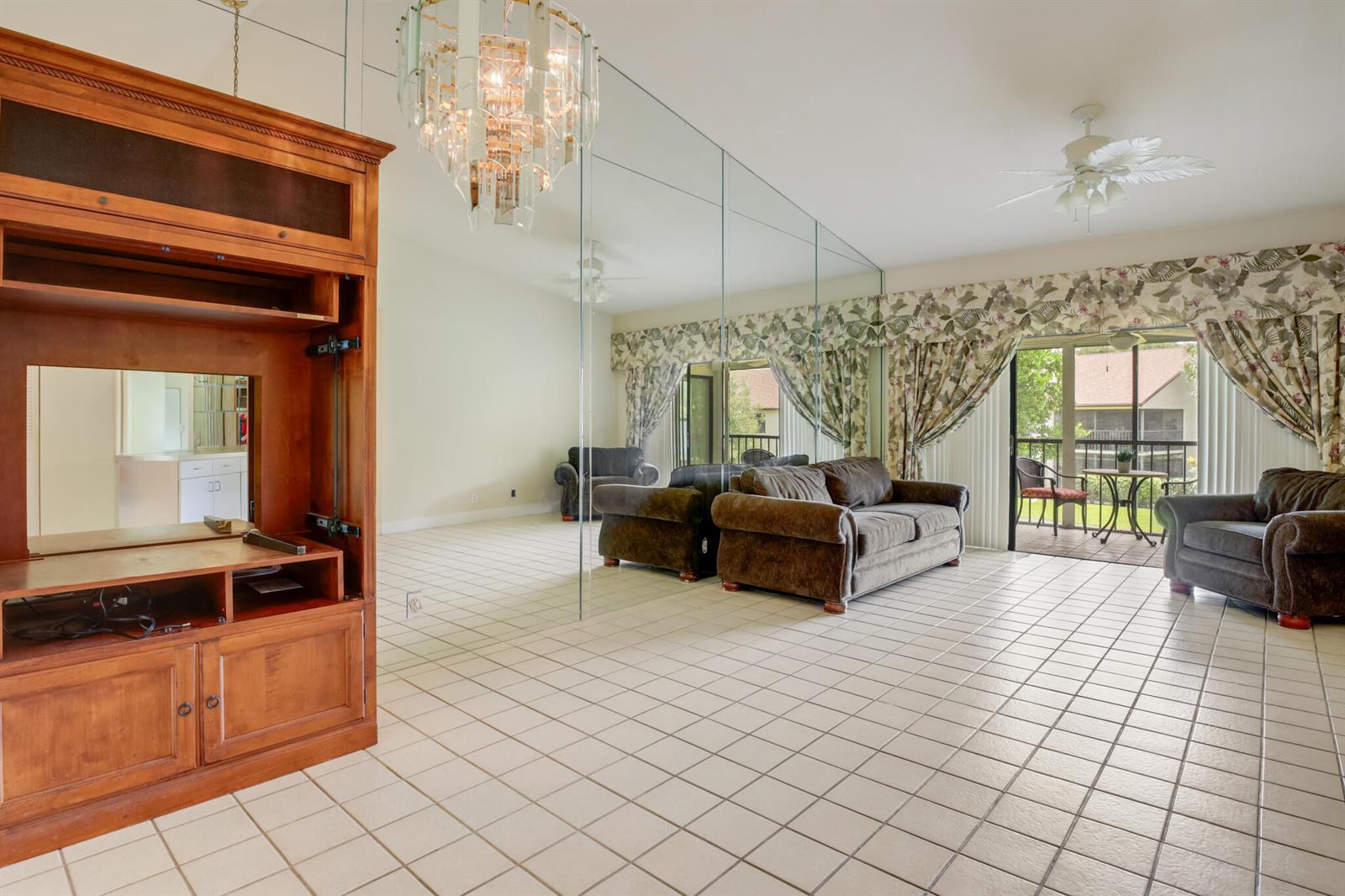 A living room features tiled floors, a mirrored wall, a wooden entertainment center, and furniture — 3340 Lucerne Park Drive, FL 33467, FL
