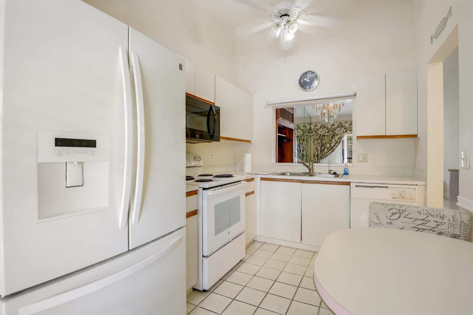 A white kitchen features a refrigerator, stove, microwave, tiled floor, and a pass-through window — 3340 Lucerne Park Drive, FL 33467, FL