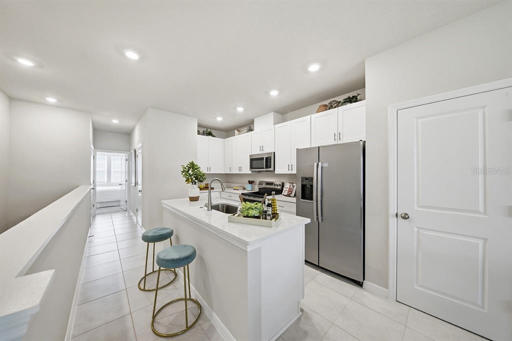 A modern kitchen features white cabinetry, stainless steel appliances, a breakfast bar, and tile flooring — 1205 WILD CREST LANE, DAYTONA BEACH, FL
