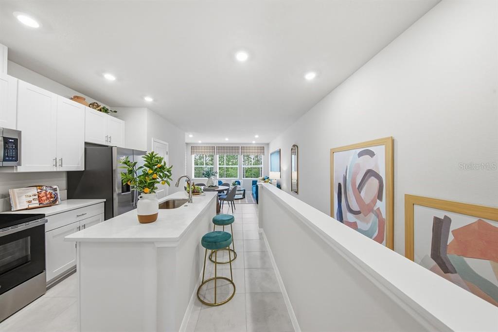 A modern kitchen with white cabinets, a quartz island, and bar stools overlooks a living area — 1205 WILD CREST LANE, DAYTONA BEACH, FL