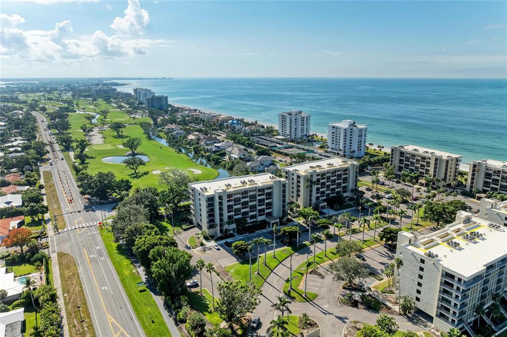 An aerial view shows multi-story apartment buildings situated between a golf course and the ocean — 1065 GULF OF MEXICO DRIVE UNIT 201, LONGBOAT KEY, FL