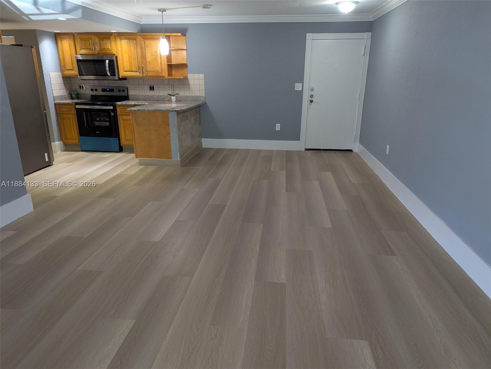 A kitchen with wooden cabinets and a gray wall opens into a spacious living area — 13700 SW 62nd St # 204, Miami FL 33183, MIAMI, FL