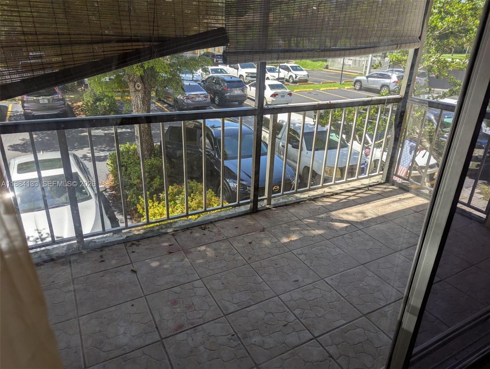 A balcony with tiled flooring overlooks a parking lot filled with various cars — 13700 SW 62nd St # 204, Miami FL 33183, MIAMI, FL