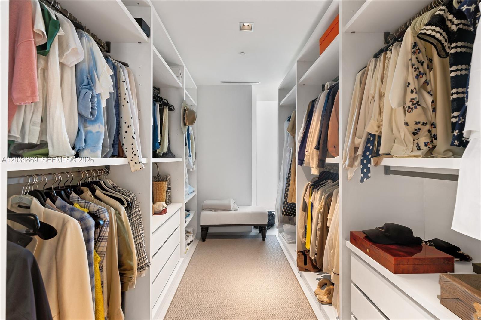A walk-in closet features white shelving, hanging clothes, and a bench at the end — 1000 Biscayne Blvd # 3701, Miami FL 33132, MIAMI, FL