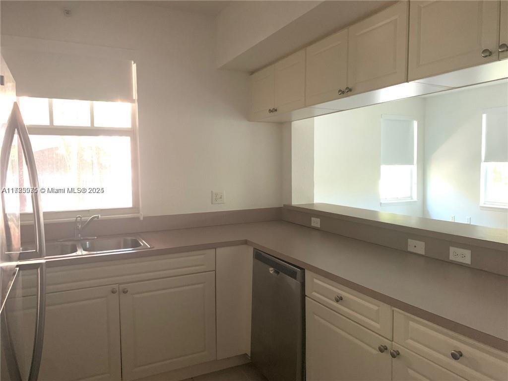 A kitchen features white cabinets, a stainless steel dishwasher, and a pass-through window — 6776 W Sample Rd # 6776, Coral Springs FL 33067, CORAL SPRINGS, FL