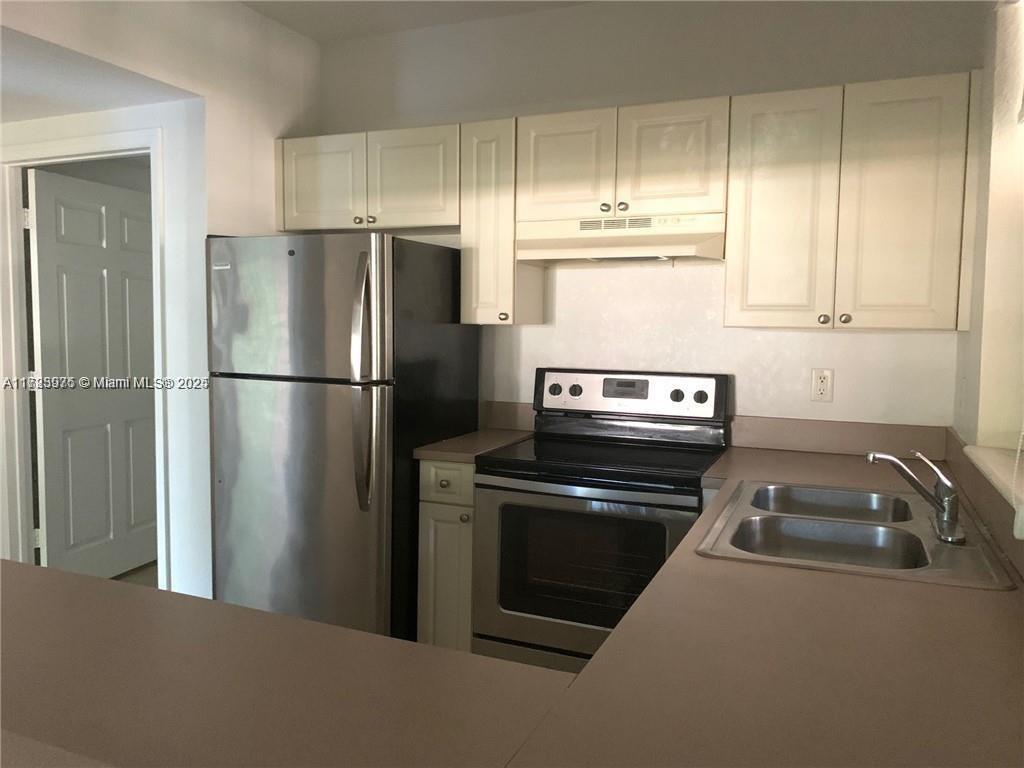 This kitchen features off-white cabinets, stainless steel appliances, and a double-basin sink — 6776 W Sample Rd # 6776, Coral Springs FL 33067, CORAL SPRINGS, FL