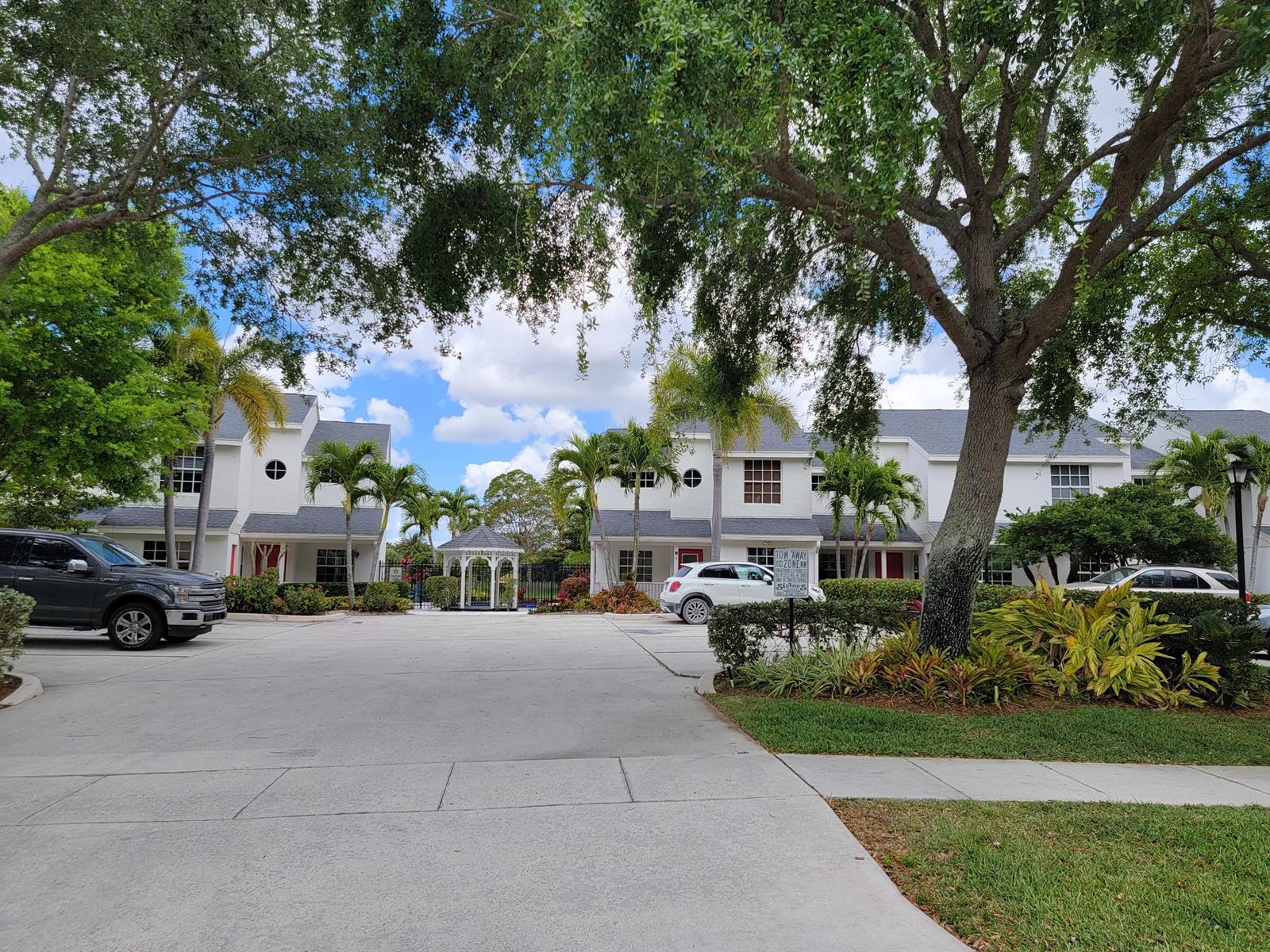 A parking lot sits in front of white two-story townhomes with a central gazebo — 12574 Westhampton Circle # I, Wellington FL 33414, WELLINGTON, FL