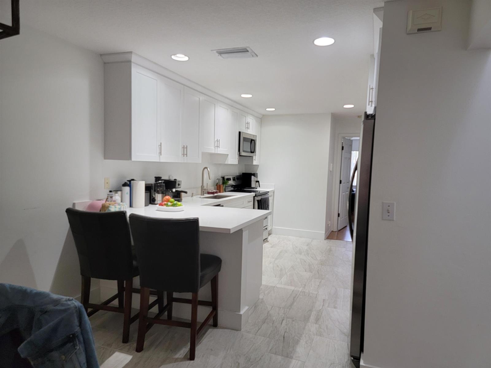 A modern kitchen features white cabinets, a breakfast bar with two chairs, and tiled flooring — 12574 Westhampton Circle # I, Wellington FL 33414, WELLINGTON, FL