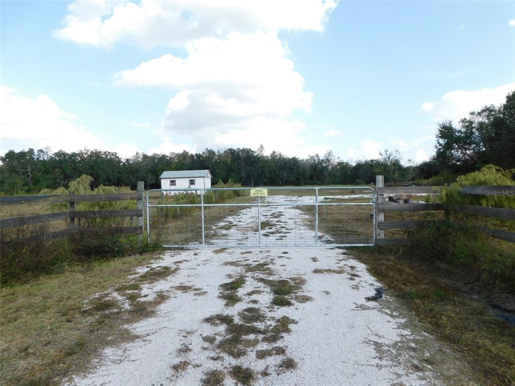 A gravel driveway leads to a metal gate and a small building on rural land — 2460 NW GARVIN AVENUE, ARCADIA, FL