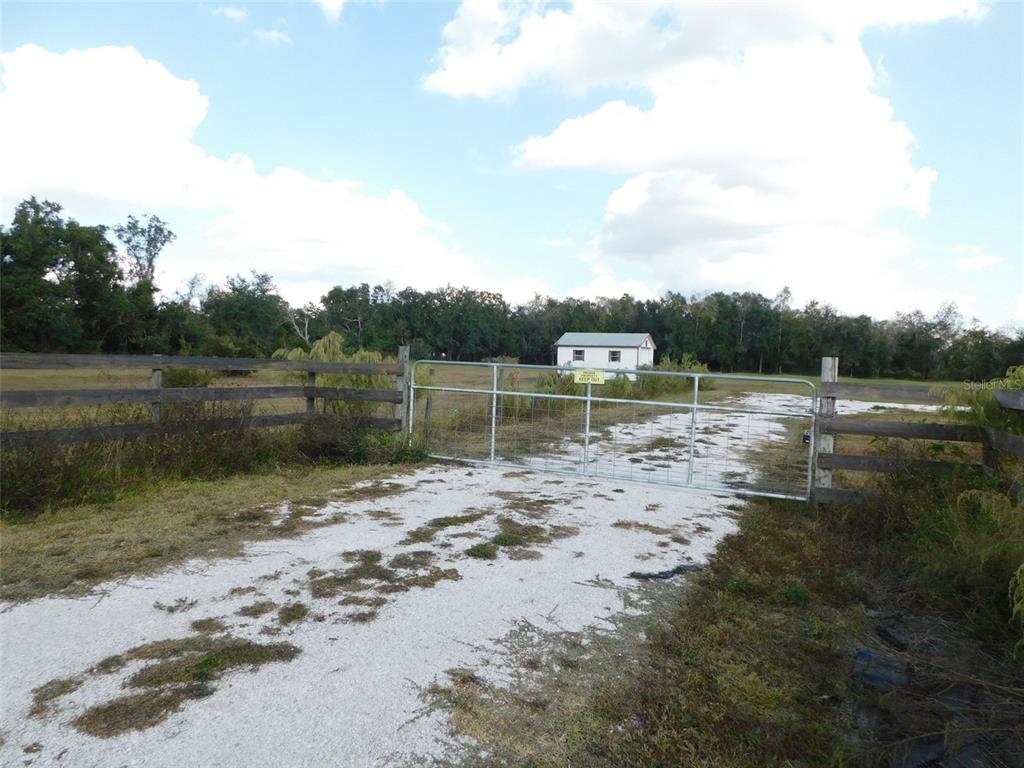 A gravel driveway leads to a metal gate and a small building on a grassy lot — 2460 NW GARVIN AVENUE, ARCADIA, FL