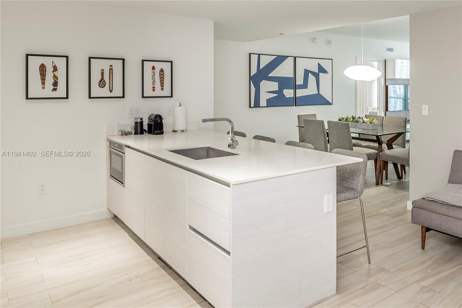 A modern kitchen island with a sink and white cabinetry sits before a dining area — 1300 S Miami Ave # 2210, Miami FL 33130, MIAMI, FL