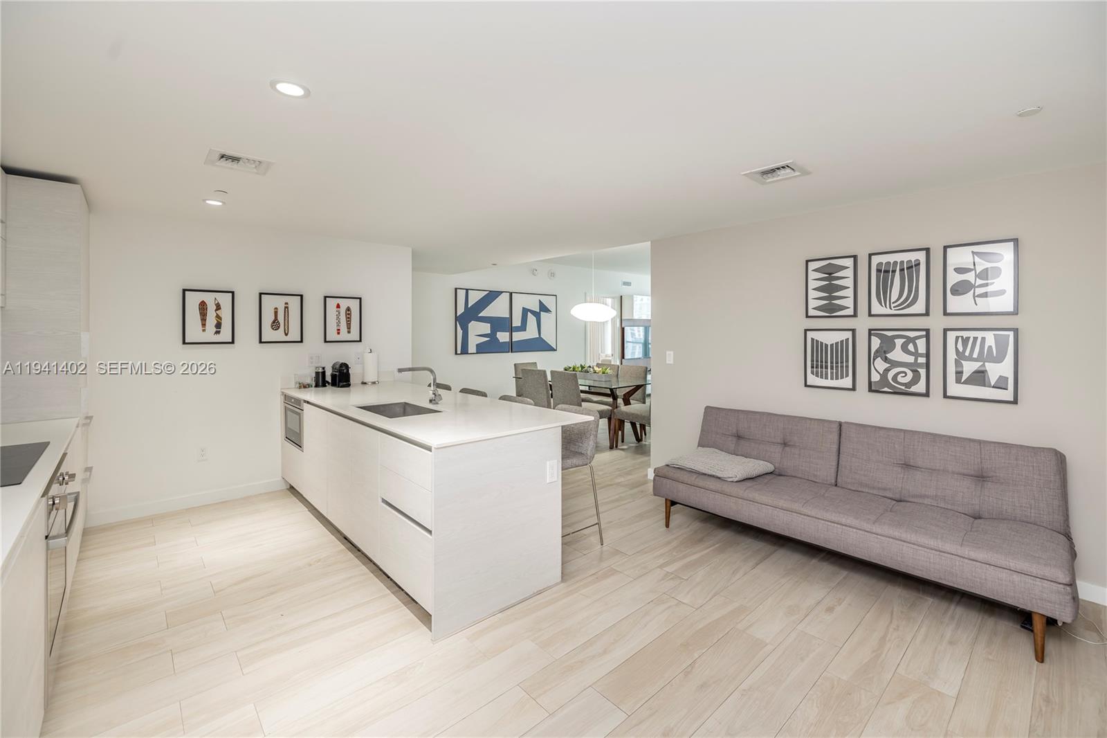 A modern kitchen with a white island and light wood flooring opens to a living area — 1300 S Miami Ave # 2210, Miami FL 33130, MIAMI, FL