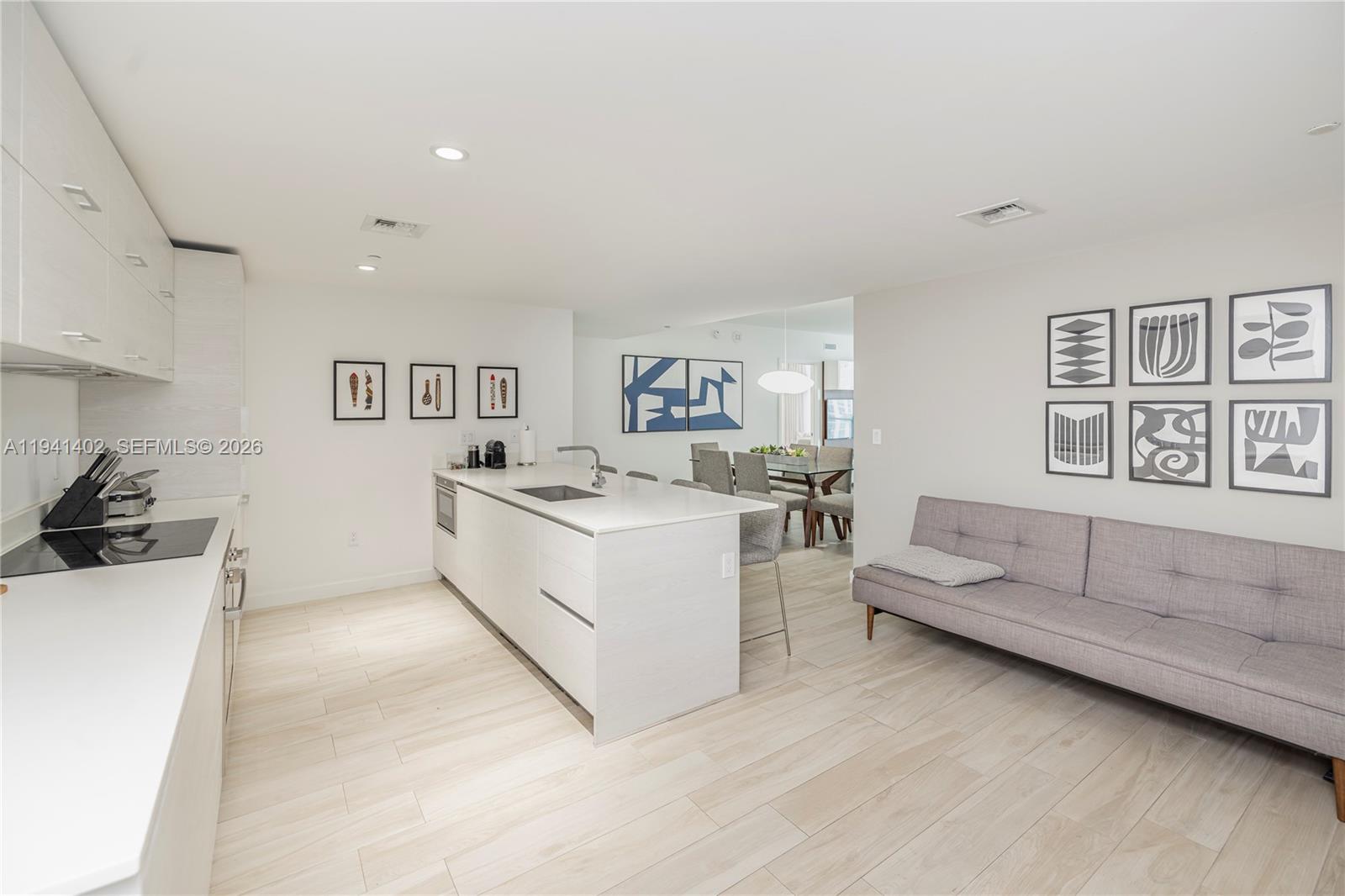 A modern kitchen with a white island and light wood floors opens to a living area — 1300 S Miami Ave # 2210, Miami FL 33130, MIAMI, FL
