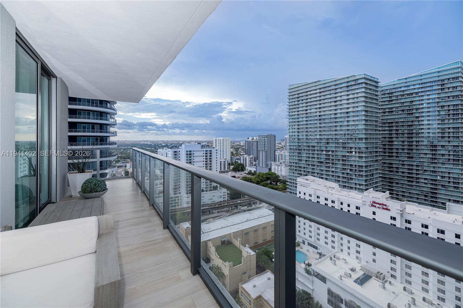A high-rise balcony with wood-look tile flooring overlooks a dense urban cityscape — 1300 S Miami Ave # 2210, Miami FL 33130, MIAMI, FL
