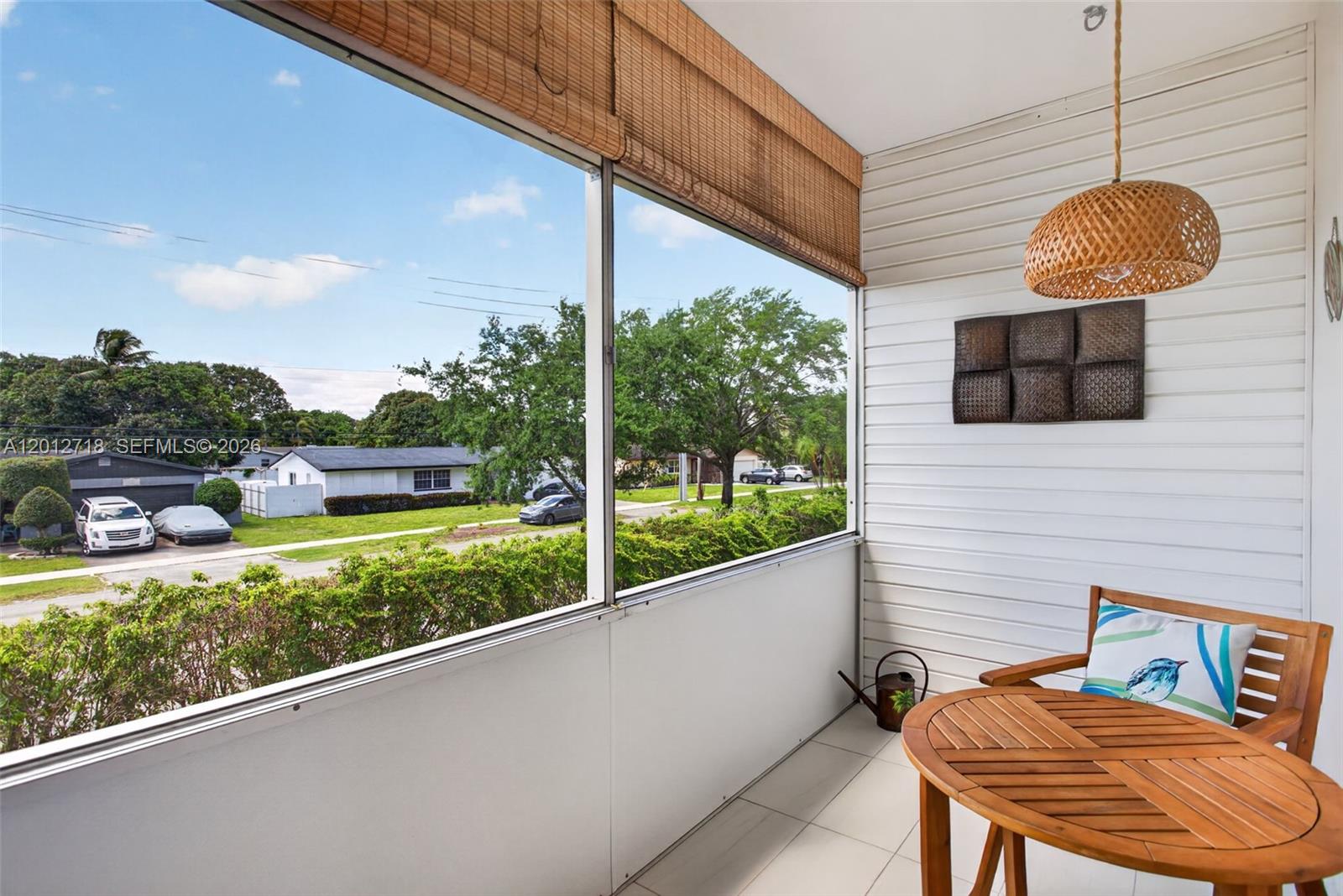 A screened-in balcony features white siding, a wooden table, and a view of a neighborhood — 4451 NW 16th St # K208, Lauderhill FL 33313, LAUDERHILL, FL