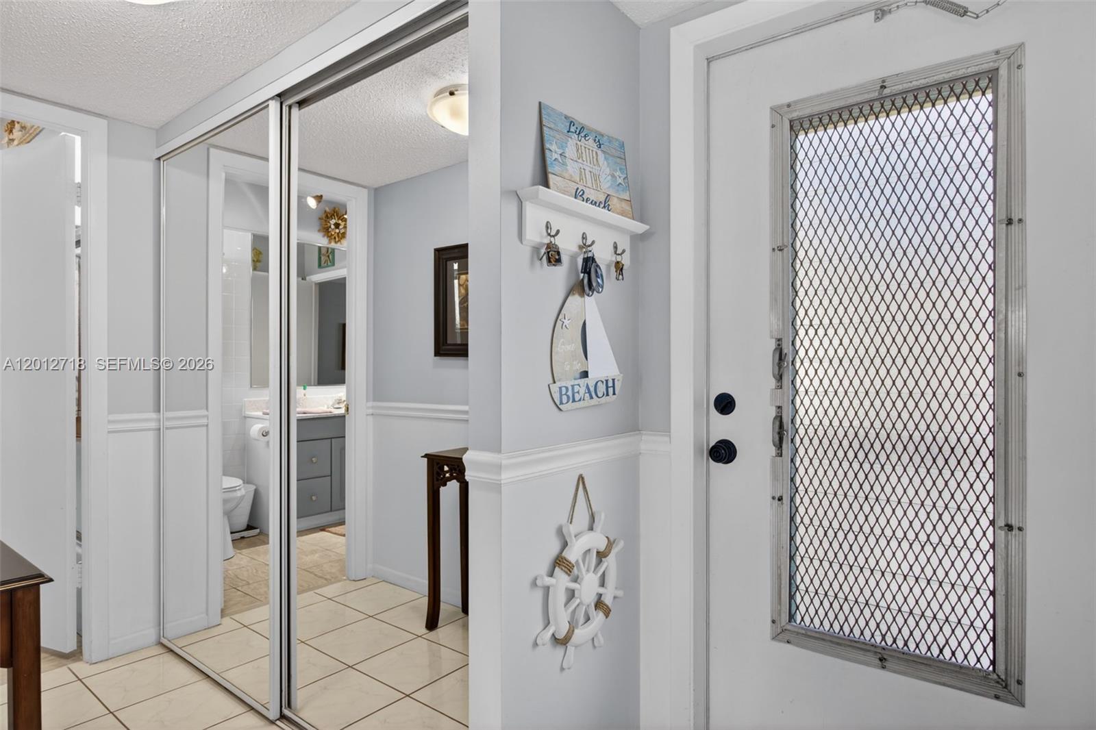 A bright entryway features a mirrored closet, a white door with a screen, and nautical decor — 4451 NW 16th St # K208, Lauderhill FL 33313, LAUDERHILL, FL