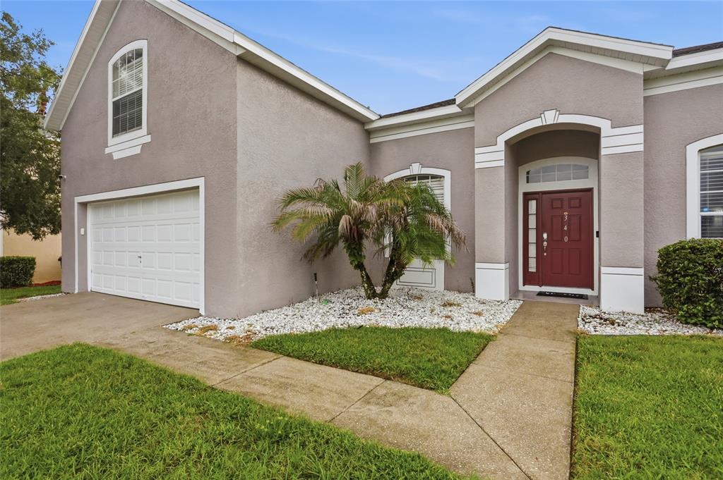 A single-story house with a gray stucco exterior, a red front door, and a garage — 340 BALLYSHANNON DRIVE, DAVENPORT, FL