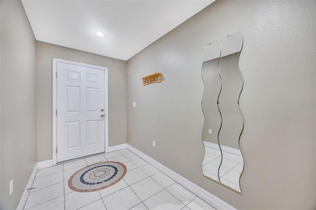 An entryway features white tile flooring, a front door, a coat rack, and wavy mirrors — 4526 BAY SPRING COURT, TAMPA, FL