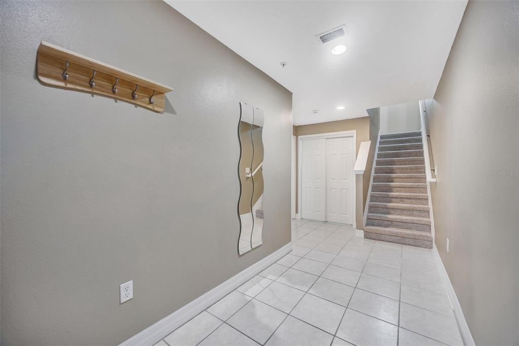 An entryway features light tile flooring, a coat rack, a wavy mirror, and carpeted stairs — 4526 BAY SPRING COURT, TAMPA, FL