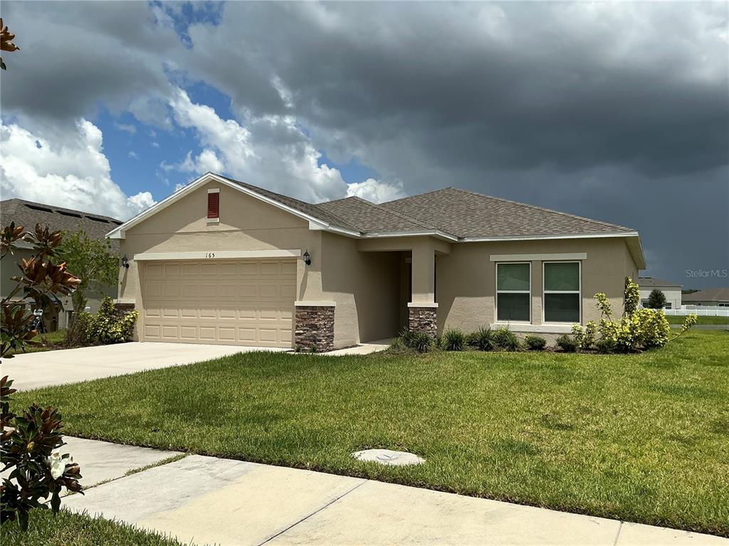 A single-story house with a beige stucco exterior, stone accents, and a two-car garage — 165 CITRINE LOOP, KISSIMMEE, FL