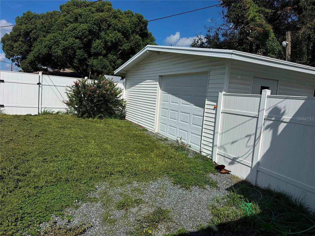 A white detached garage sits in a backyard next to a white vinyl privacy fence — 5829 12TH STREET, ZEPHYRHILLS, FL