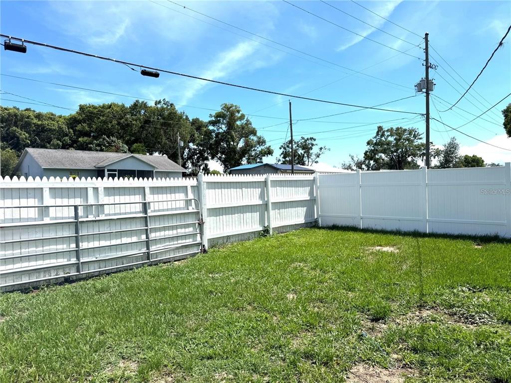 A fenced backyard features a metal gate and a white vinyl privacy fence — 5829 12TH STREET, ZEPHYRHILLS, FL