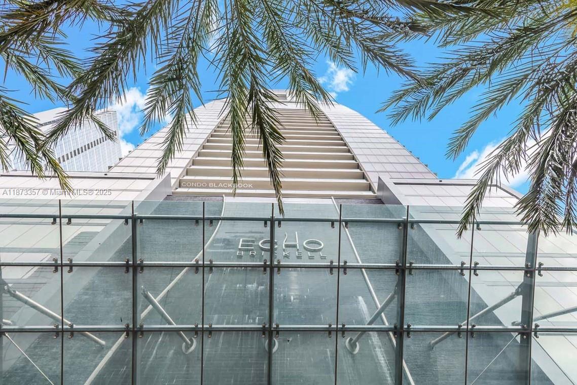 A low-angle view of the Echo Brickell skyscraper exterior with palm fronds in the foreground — 1451 Brickell Ave # 2706, Miami FL 33131, MIAMI, FL