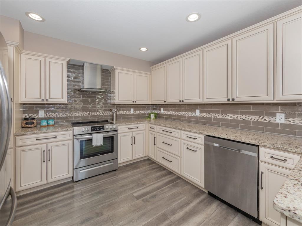 A kitchen features cream cabinets, granite countertops, stainless steel appliances, and a gray tiled backsplash — 21004 ISOLA BELLA CIRCLE, VENICE, FL
