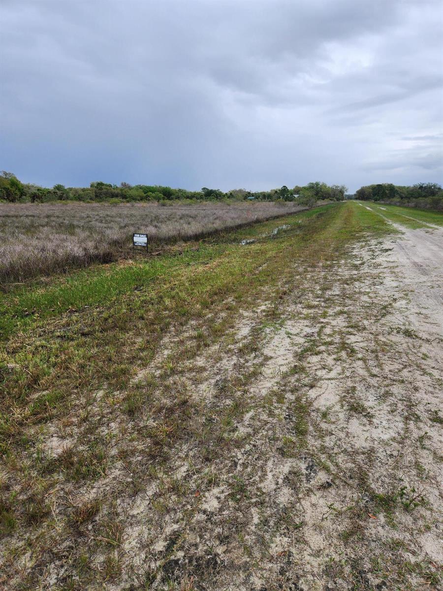 A dirt road runs alongside a large, flat, grassy lot with a for sale sign — 15679 NW 296th Street, Okeechobee FL 34972, OKEECHOBEE, FL