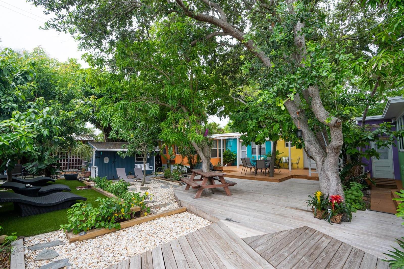 A backyard features a wooden deck, a picnic table, gravel landscaping, and colorful small buildings — 1944 NE 5th Street, Deerfield Beach FL 33441, DEERFIELD BEACH, FL