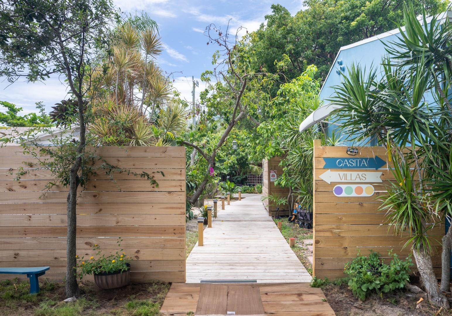 A wooden boardwalk leads through a gated entrance toward lush greenery and tropical landscaping — 1944 NE 5th Street, Deerfield Beach FL 33441, DEERFIELD BEACH, FL