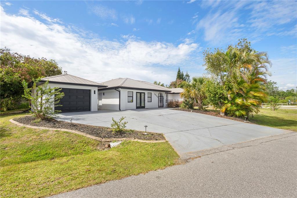 A single-story white house with a black garage door and a large concrete driveway — 19723 MIDWAY BOULEVARD, PORT CHARLOTTE, FL