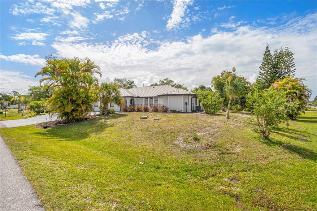 A white single-story house with a metal roof sits on a grassy lot with palm trees — 19723 MIDWAY BOULEVARD, PORT CHARLOTTE, FL