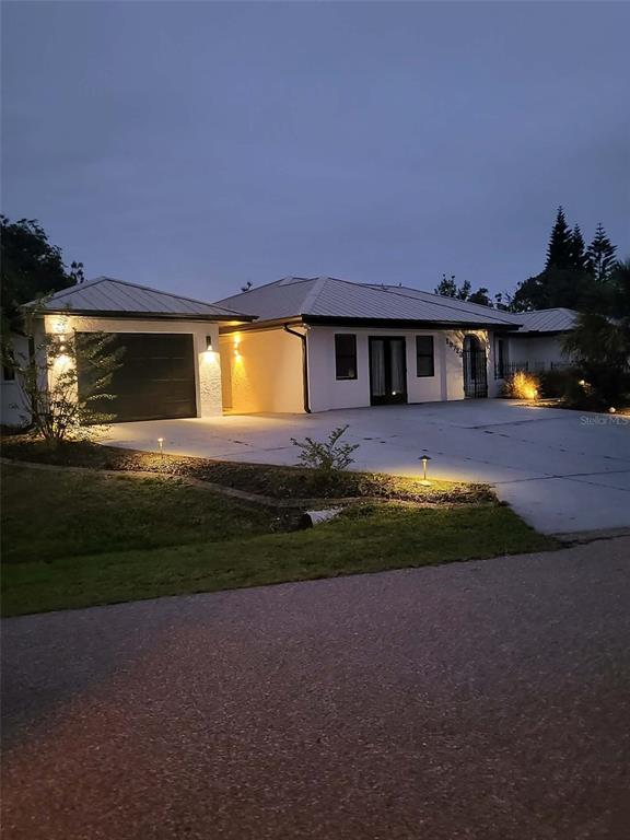 A single-story house with a metal roof and attached garage sits at dusk — 19723 MIDWAY BOULEVARD, PORT CHARLOTTE, FL
