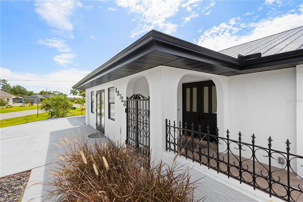 A white stucco house exterior features a black metal gate and a covered porch area — 19723 MIDWAY BOULEVARD, PORT CHARLOTTE, FL