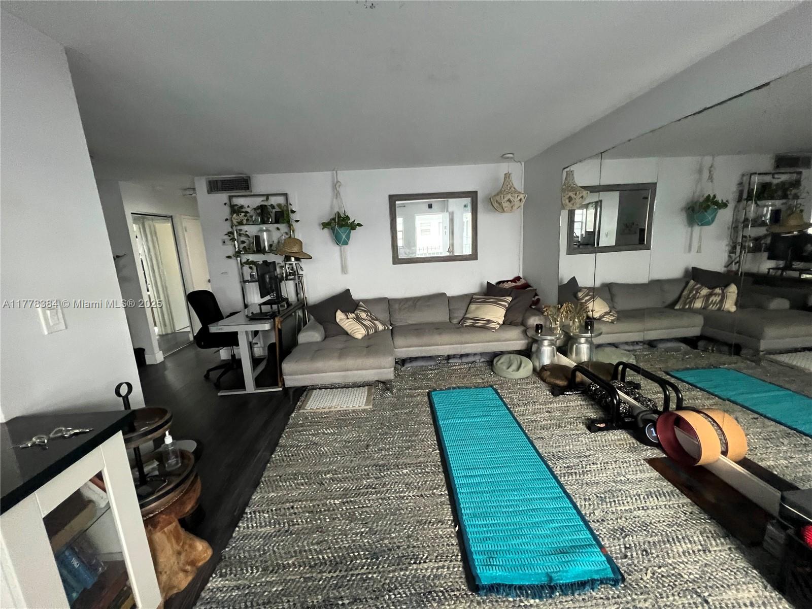 A living room features a gray sectional sofa, a large area rug, and a mirrored wall — 221 Meridian Ave # 206, Miami Beach FL 33139, MIAMI BEACH, FL