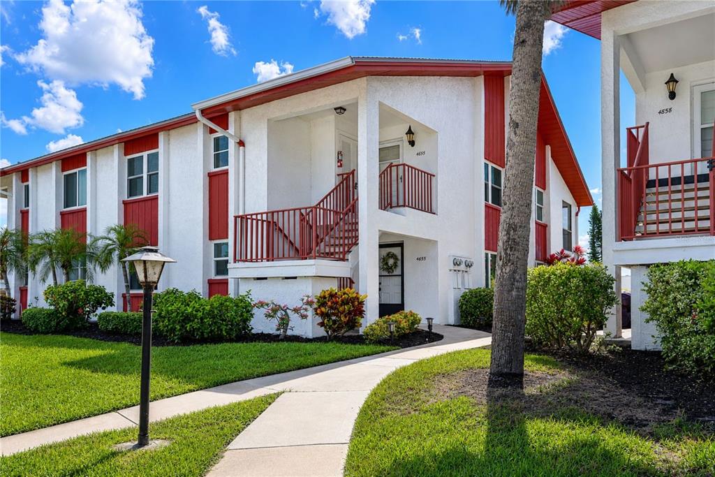 A two-story apartment building with white stucco walls, red accents, and an exterior staircase — 4853 INDEPENDENCE DRIVE, BRADENTON, FL
