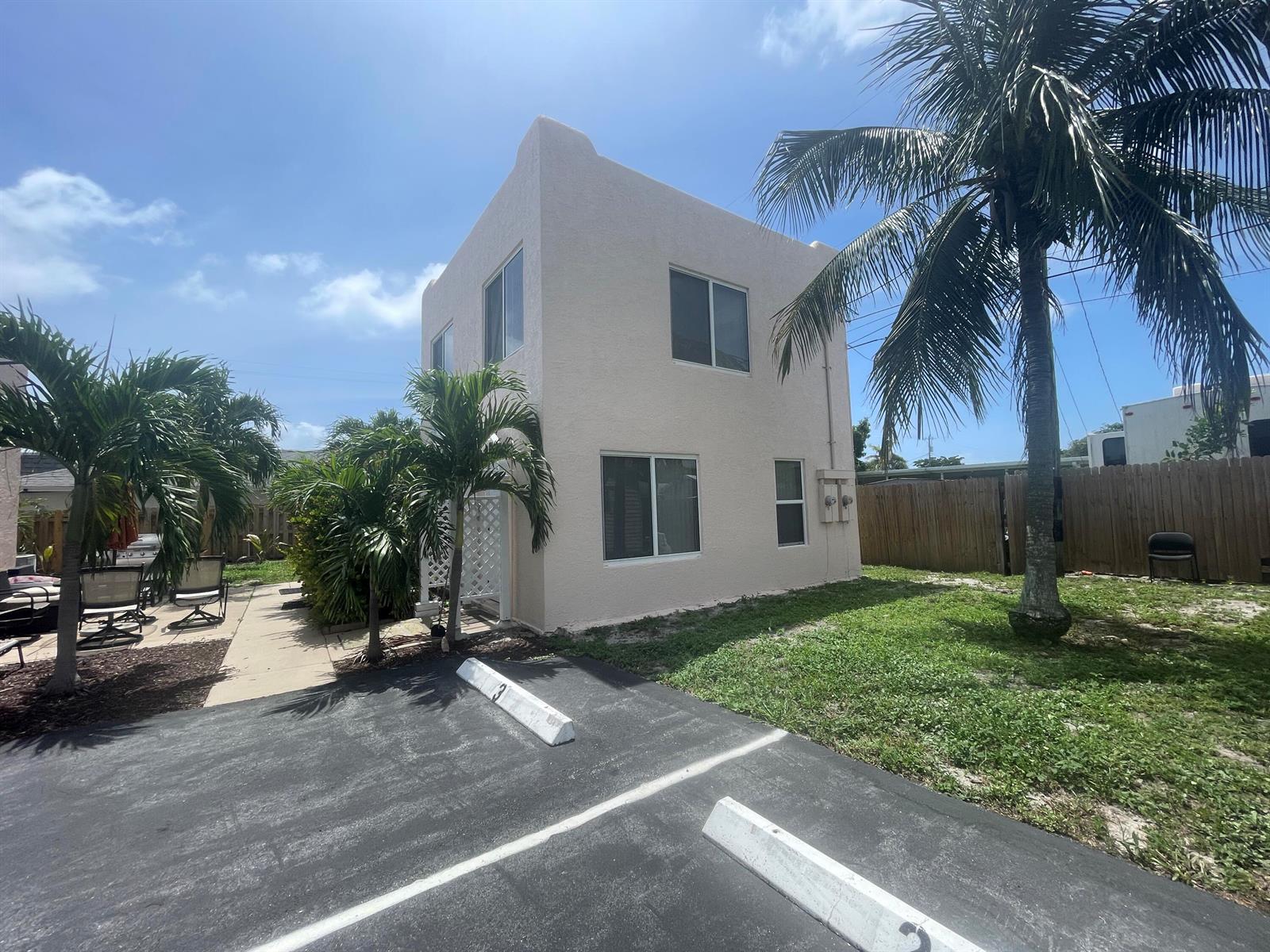 A two-story stucco building stands next to a parking lot with palm trees and fencing — 505 24th Avenue N, FL 33460, FL